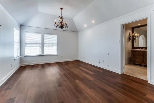 an empty room with wooden floor chandelier and windows