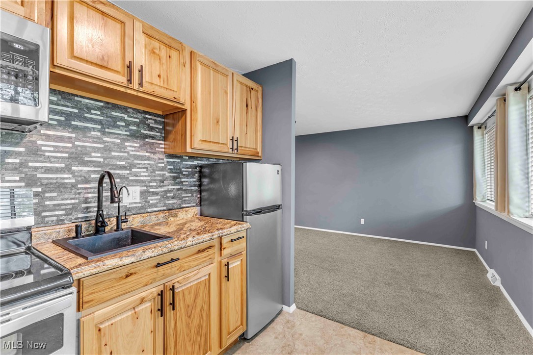 6640 Pearl Road, Unit 104 Cleveland, OH 44130 - Photo 8 of 31 Kitchen with stainless steel appliances, a sink, light colored carpet, backsplash, and light brown cabinetry