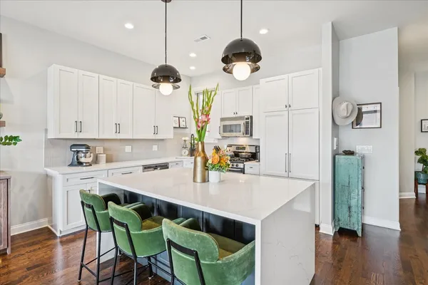 a kitchen with kitchen island a stove a chandelier a dining table and chairs with wooden floor