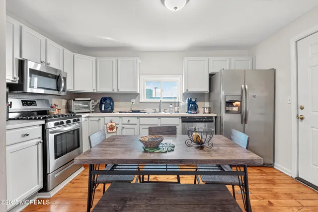 a kitchen with stainless steel appliances granite countertop a stove a refrigerator a sink a dining table and chairs with white cabinets