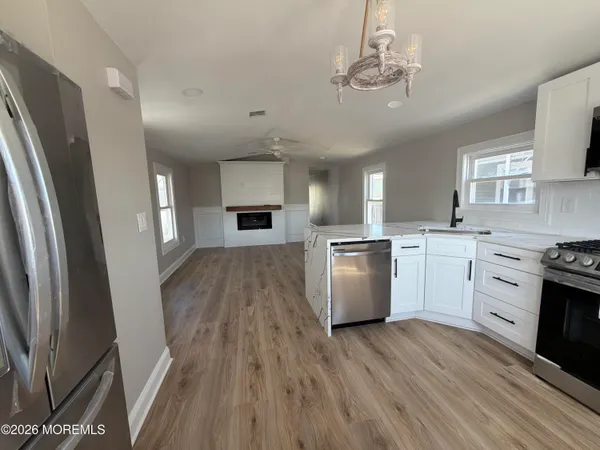 a kitchen with granite countertop a refrigerator a sink dishwasher a stove and white cabinets with wooden floor