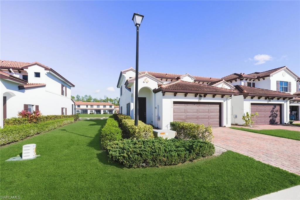 View of front facade with a front lawn, stucco siding, decorative driveway, a tiled roof, and an attached garage