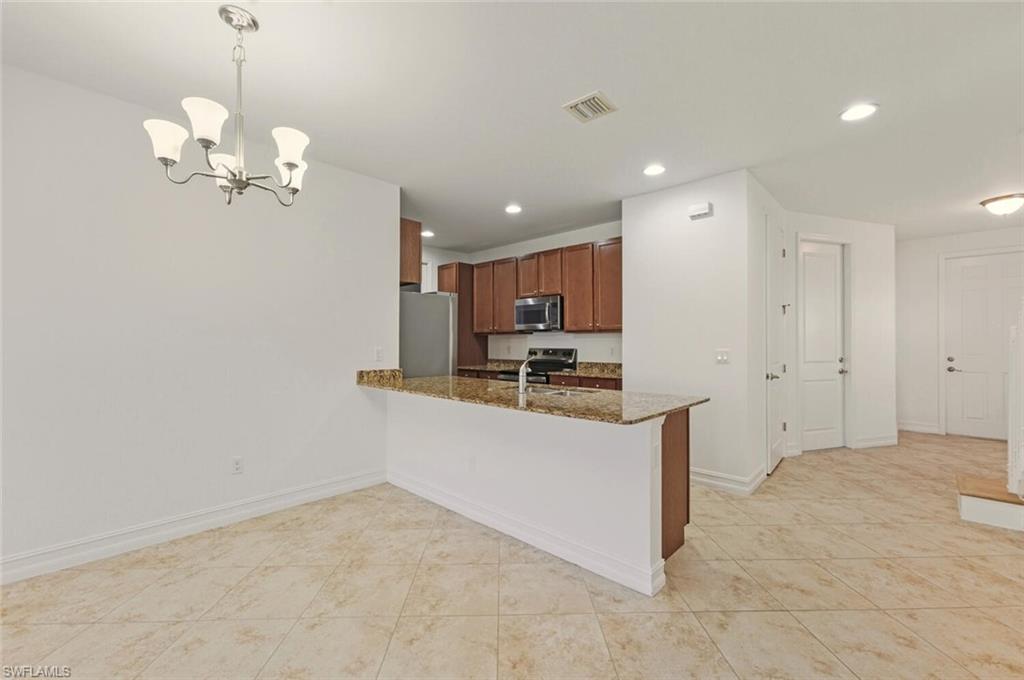 7770 Bristol Circle Naples, FL 34120 - Photo 5 of 36 Kitchen with brown cabinets, decorative light fixtures, a peninsula, appliances with stainless steel finishes, and dark stone counters