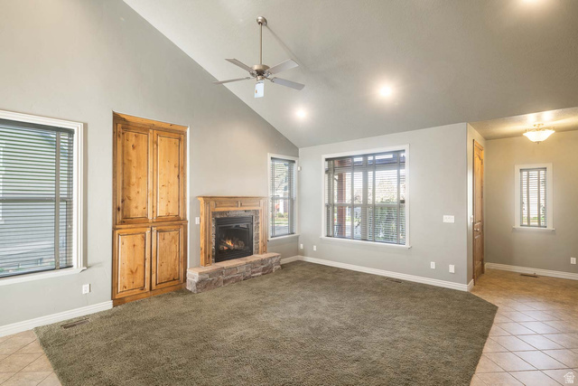 1997 West Cres Drive Mapleton, UT 84664 - Photo 9 of 35 Unfurnished living room featuring light tile patterned floors, a ceiling fan, lofted ceiling, a stone fireplace, and healthy amount of natural light