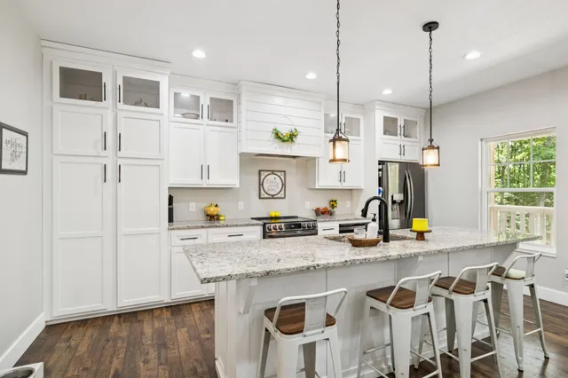 a kitchen with granite countertop stainless steel appliances a refrigerator a sink a stove a counter space and wooden floor