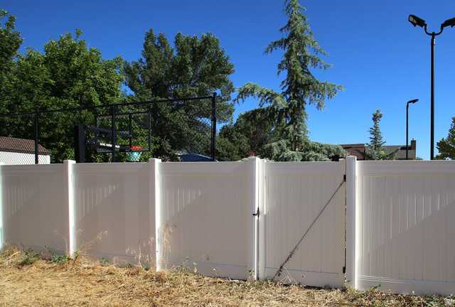 1612 East 450 South Springville, UT 84663 - Photo 8 of 48 Outdoor area featuring a white privacy fence with a functional gate, complemented by mature perimeter trees and a visible basketball hoop structure beyond the fence