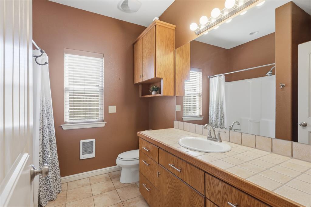 207 Dennis Road Lipan, TX 76462 - Photo 25 of 40 Warm-toned bathroom featuring a tile-top vanity with integrated sink, wood-finish cabinetry, and a full-width mirror