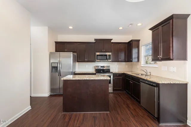 a kitchen with stainless steel appliances granite countertop wooden cabinets a refrigerator a stove a sink and a microwave with wooden floor