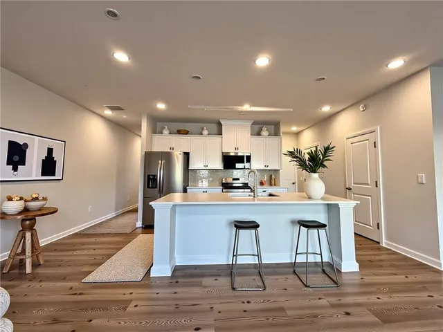 a kitchen with stainless steel appliances kitchen island granite countertop a dining table chairs sink and wooden floor