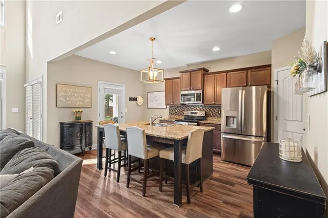 a kitchen with stainless steel appliances granite countertop a refrigerator a stove a sink a dining table and chairs with wooden floor