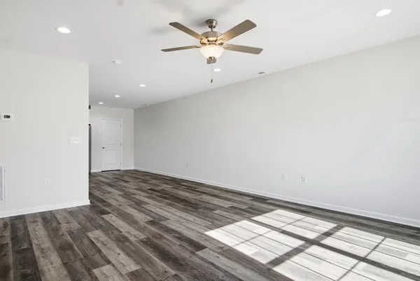 a view of an empty room with wooden floor and a ceiling fan
