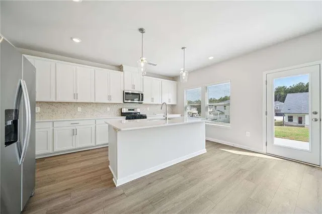 a kitchen with stainless steel appliances granite countertop a refrigerator a sink dishwasher a stove and white cabinets with wooden floor