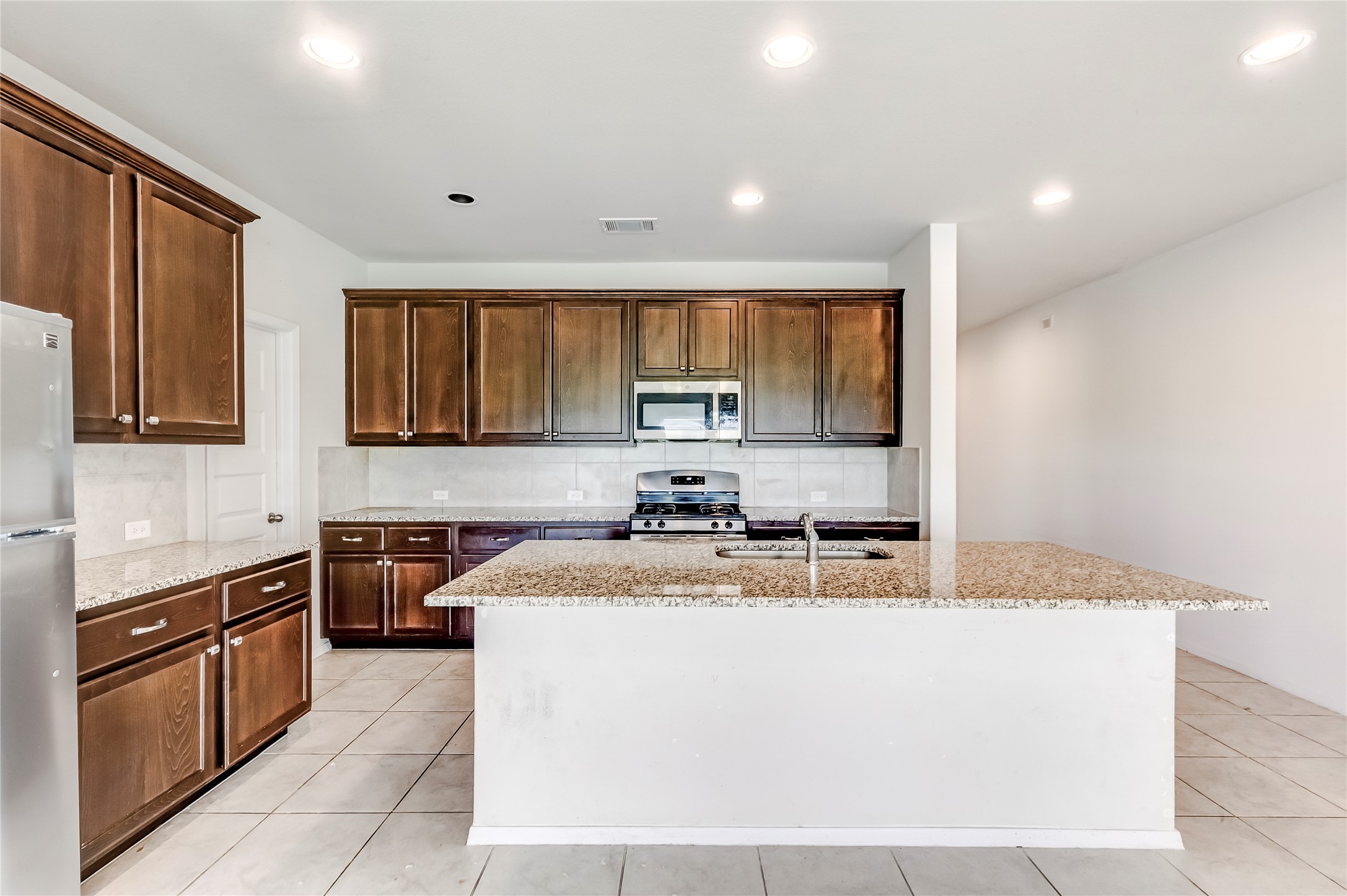 2721 Winding Creek Road Kyle, TX 78640 - Photo 9 of 27 Kitchen with granite countertops, wood cabinetry, tile flooring, stainless steel appliances, and an island with a sink