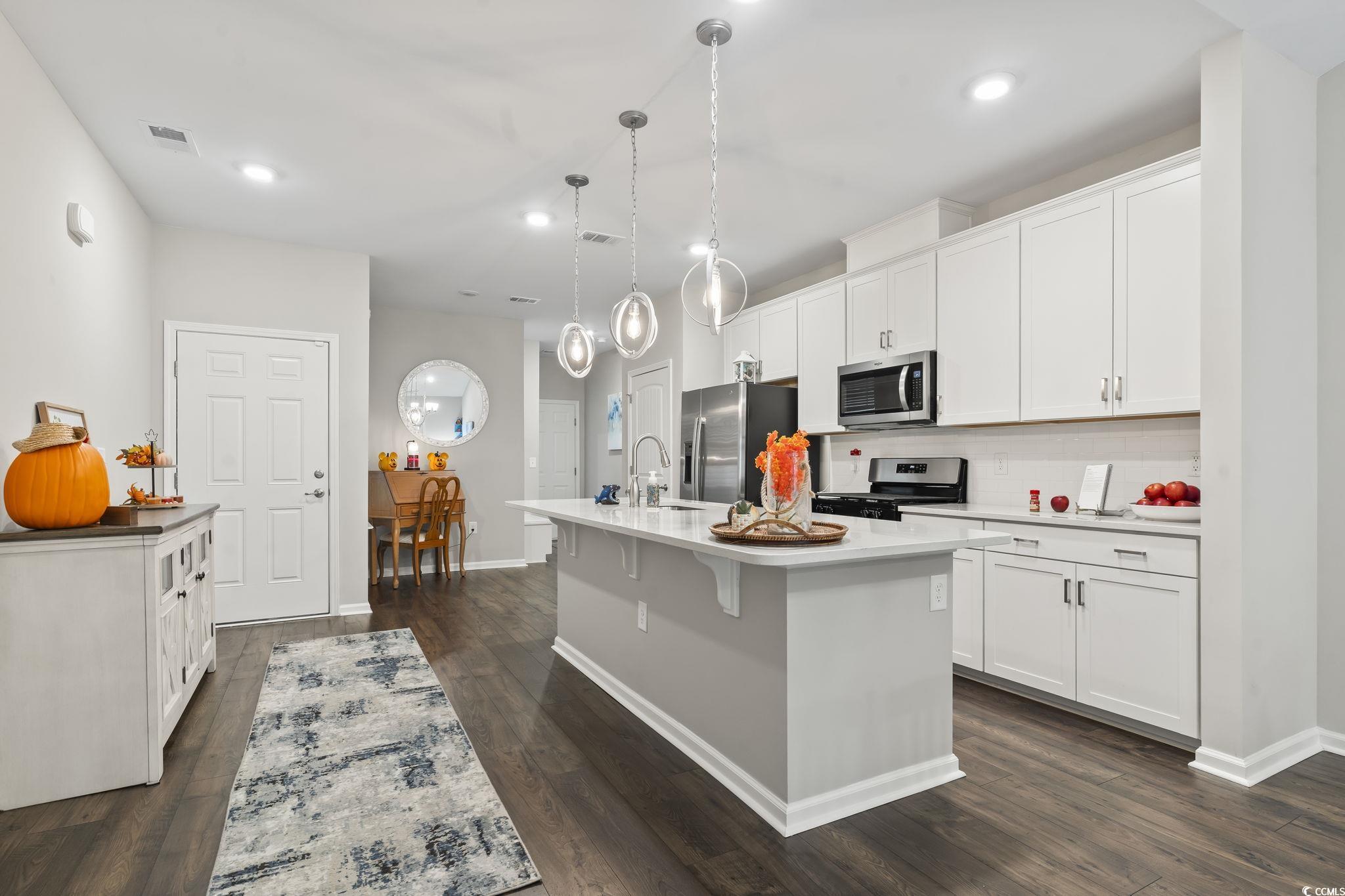 4040 Taranto Loop, Unit 5303C Myrtle Beach, SC 29579 - Photo 10 of 38 Kitchen featuring white cabinetry, stainless steel appliances, a center island with sink, decorative backsplash, and dark wood-type flooring