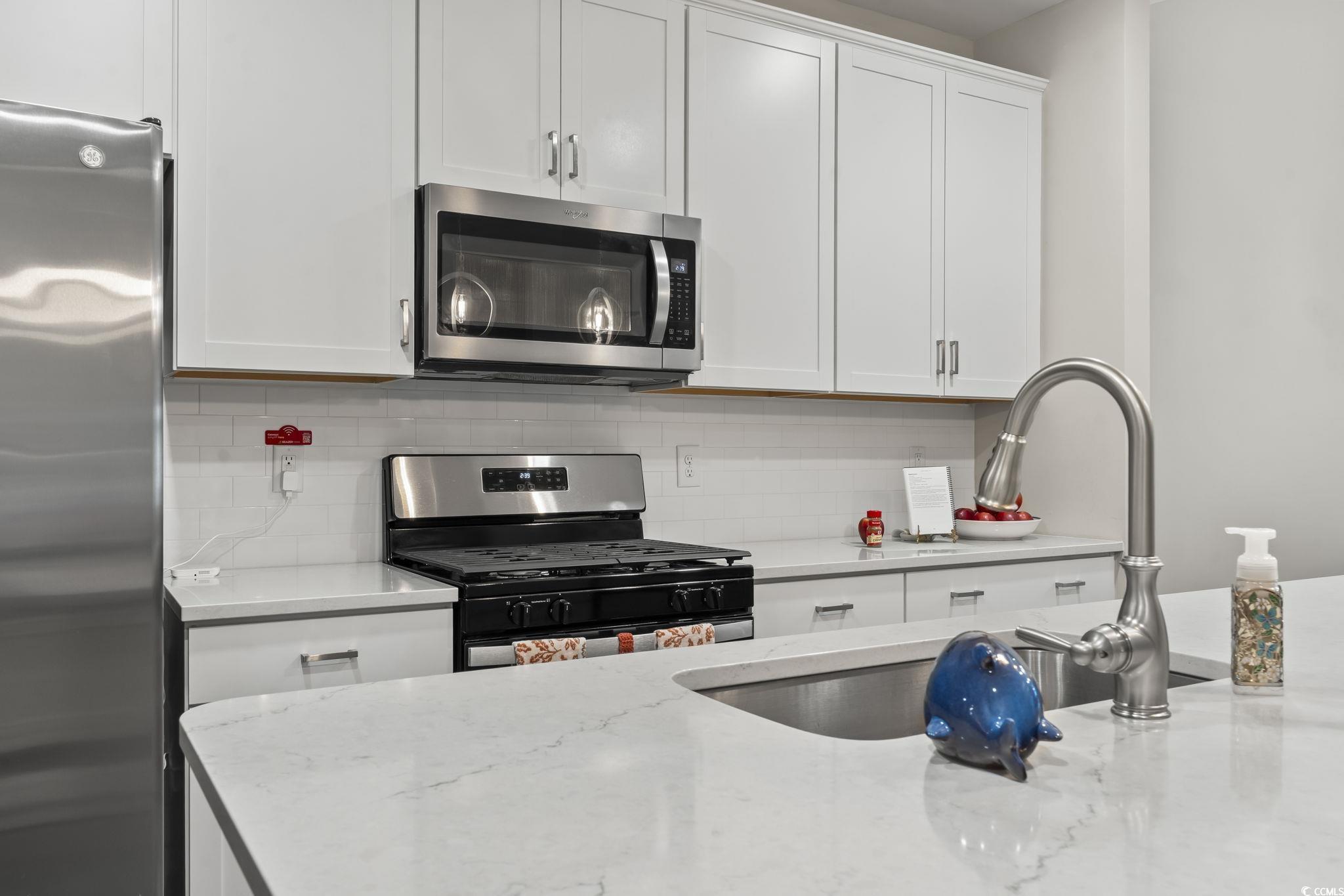 4040 Taranto Loop, Unit 5303C Myrtle Beach, SC 29579 - Photo 8 of 38 Kitchen featuring stainless steel appliances, white cabinets, light stone countertops, and decorative backsplash