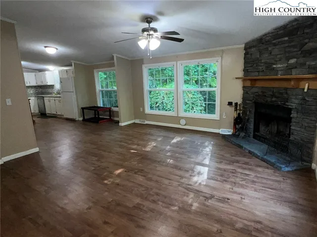an empty room with windows fireplace and a kitchen view
