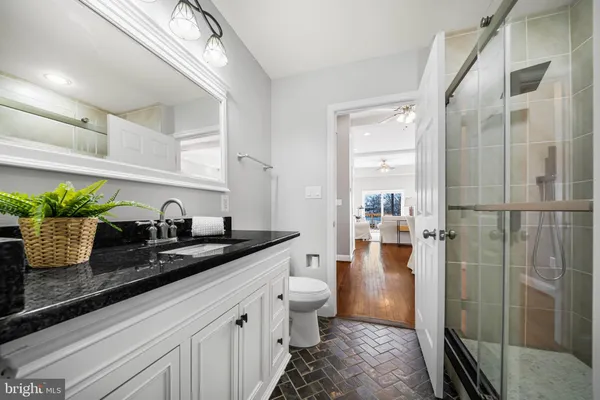 a bathroom with a granite countertop sink a toilet a mirror and shower