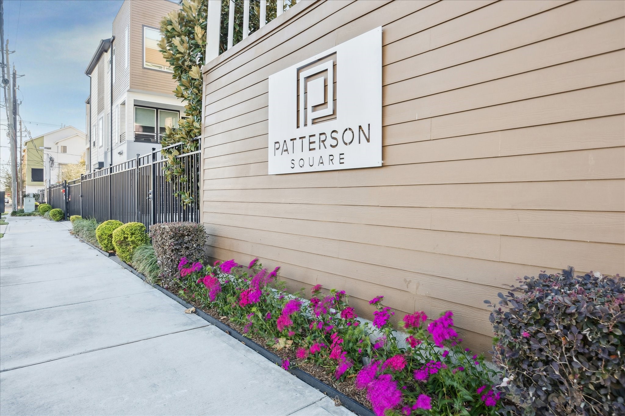 1603 Patterson Street, Unit E Houston, TX 77007 - Photo 2 of 32 This photo showcases the entrance to Patterson Square, featuring a modern design with a wooden exterior and a well-maintained garden along a paved walkway. The area is inviting, with colorful flowers and neatly trimmed shrubs enhancing the curb appeal.