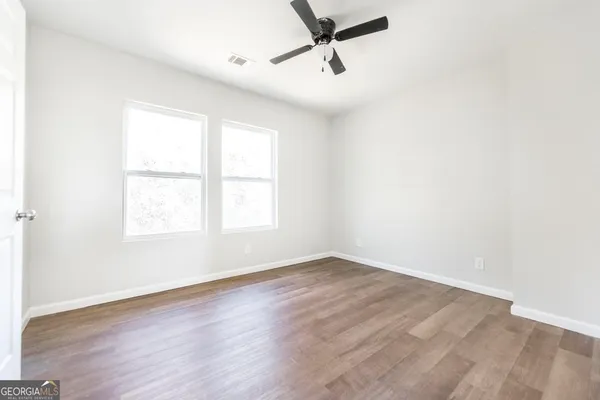 an empty room with wooden floor fan and windows