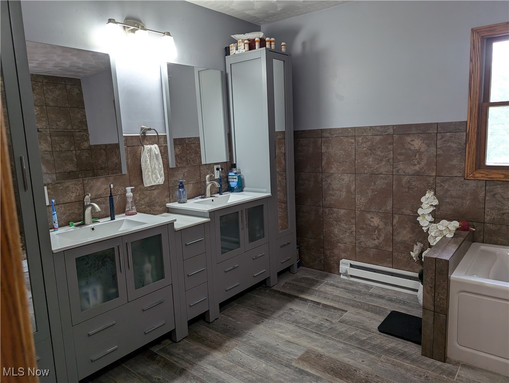 46136 Carlisle Road Lisbon, OH 44432 - Photo 38 of 48 Bathroom with a tub to relax in, vanity, a baseboard radiator, tile walls, and hardwood / wood-style flooring