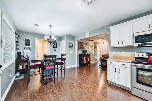 a kitchen with stainless steel appliances a stove a sink a dining table and chairs with wooden floor