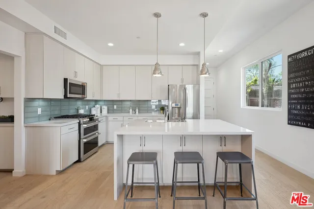 a kitchen with stainless steel appliances kitchen island granite countertop a dining table chairs sink and microwave