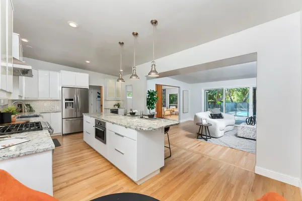 a kitchen with a stove a sink and white cabinets with wooden floor