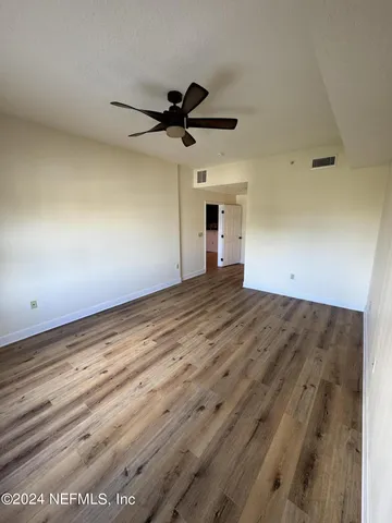 an empty room with wooden floor a ceiling fan and windows