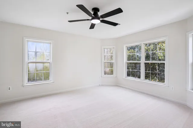 an empty room with chandelier fan and windows