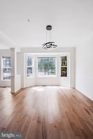 an empty room with wooden floor chandelier and windows