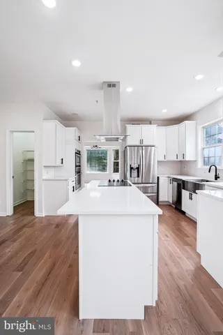 a kitchen with kitchen island a stove a sink a refrigerator and white cabinets with wooden floor
