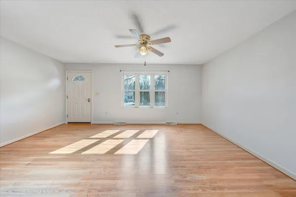 an empty room with wooden floor chandelier fan and windows