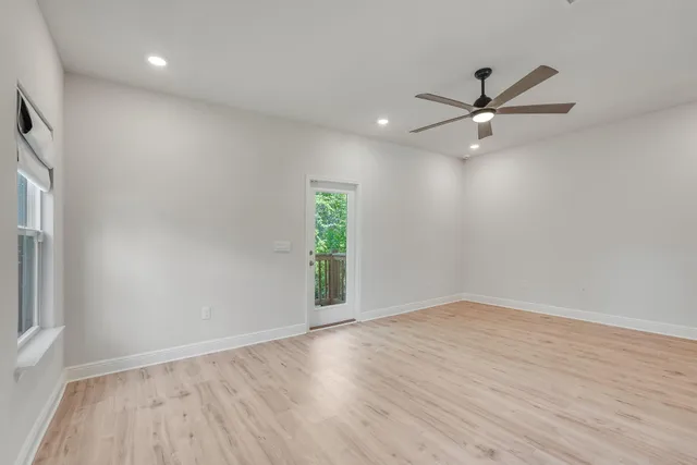 an empty room with wooden floor a ceiling fan and windows