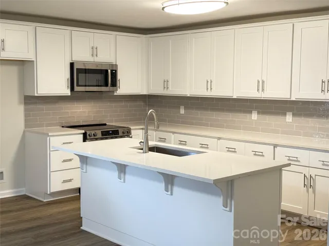 a kitchen with stainless steel appliances granite countertop a sink stove and white cabinets with wooden floor