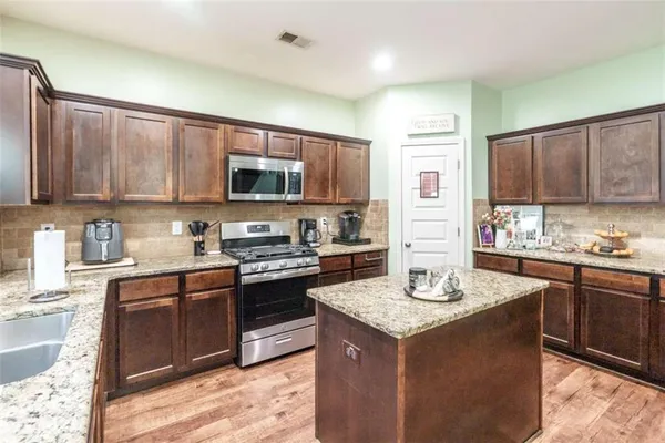 a kitchen with granite countertop kitchen island stainless steel appliances a sink stove and cabinets