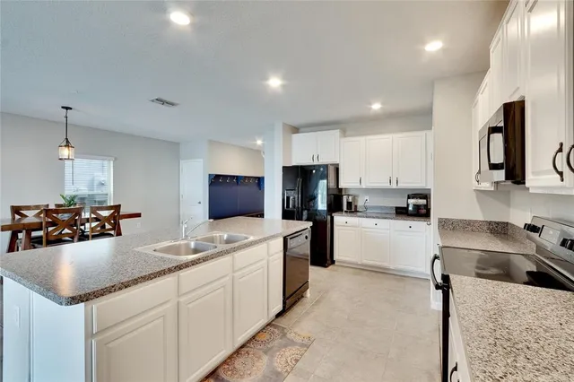 a kitchen with stainless steel appliances kitchen island granite countertop a dining table chairs and a refrigerator