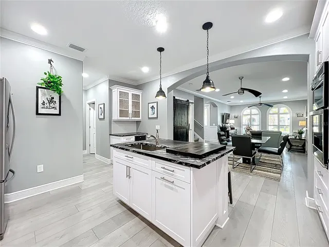 a kitchen with stainless steel appliances kitchen island granite countertop a stove a sink dishwasher a refrigerator and white cabinets with wooden floor
