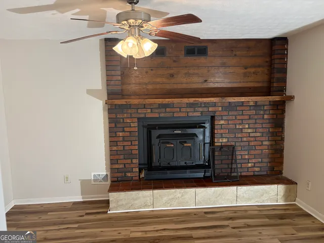 a view of a livingroom with a fireplace a ceiling fan and wooden floor