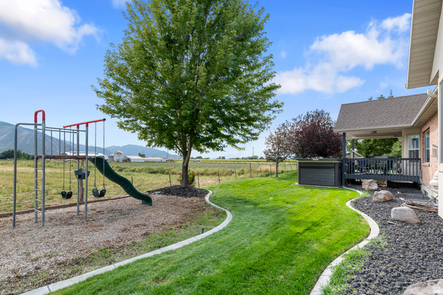 1501 West Elk Circle Mapleton, UT 84664 - Photo 6 of 39 Expansive backyard featuring a manicured lawn, landscaping with decorative rock and boulders, a covered patio, and a dedicated play area with a swing set