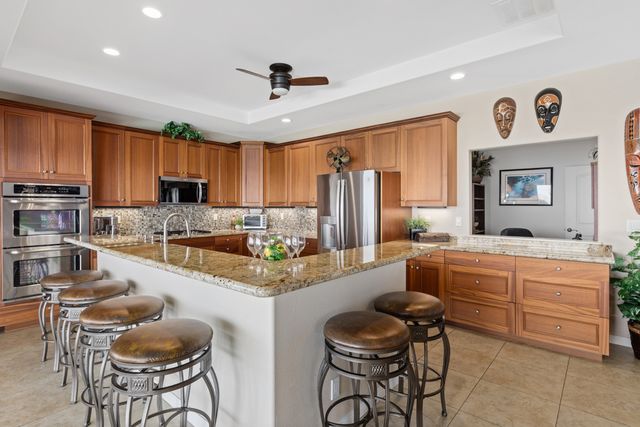 a large kitchen with kitchen island granite countertop a stove a sink a dining table and chairs with wooden cabinets