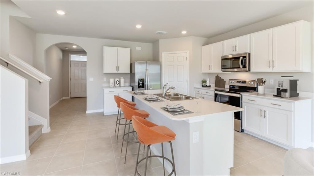 17764 Shade Tree Loop Punta Gorda, FL 33982 - Photo 3 of 12 Kitchen featuring stainless steel appliances, white cabinetry, arched walkways, light tile patterned floors, and an island with sink