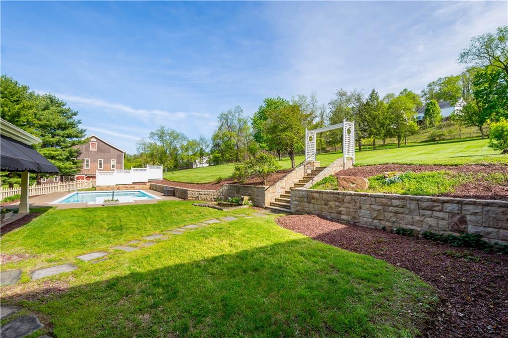 571 West McMurray Road Canonsburg, PA 15317 - Photo 41 of 47 A beautiful perspective of the manicured grounds featuring professional stonework and tiered landscaping. This view showcases the elegant stone retaining walls and steps that lead from the pool area to the upper level of the 14-acre estate, all framed by a charming white arbor and mature trees.