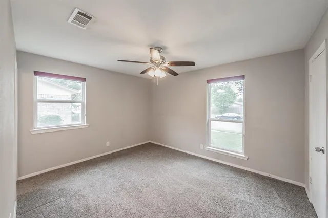 an empty room that has a chandelier fan and a large window