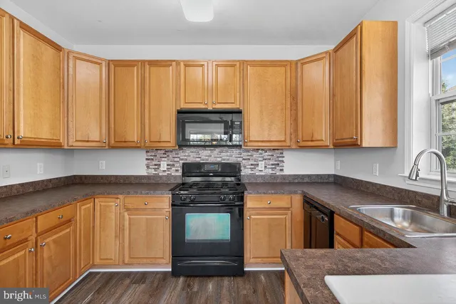 a kitchen with granite countertop a stove a sink and dishwasher wooden cabinets with wooden floor