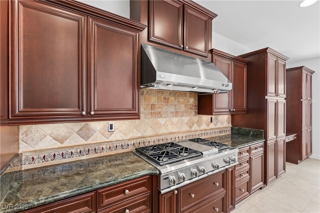 58 Contrada Fiore Drive Henderson, NV 89011 - Photo 11 of 56 Kitchen featuring under cabinet range hood, dark stone counters, stainless steel gas stovetop, and tasteful backsplash