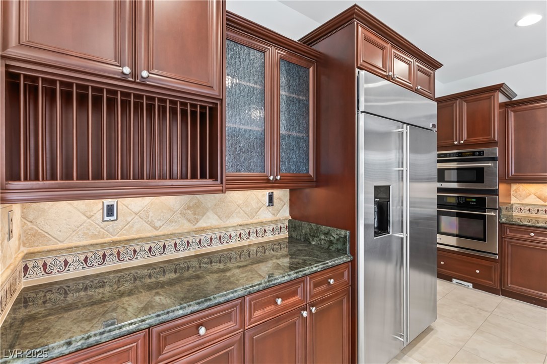 58 Contrada Fiore Drive Henderson, NV 89011 - Photo 14 of 56 Kitchen with decorative backsplash, appliances with stainless steel finishes, dark stone counters, light tile patterned floors, and glass insert cabinets