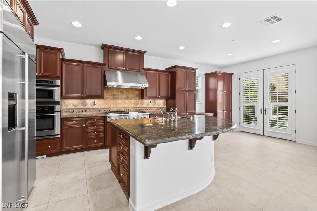 58 Contrada Fiore Drive Henderson, NV 89011 - Photo 15 of 56 Kitchen featuring decorative backsplash, dark stone counters, a breakfast bar, stainless steel appliances, and recessed lighting