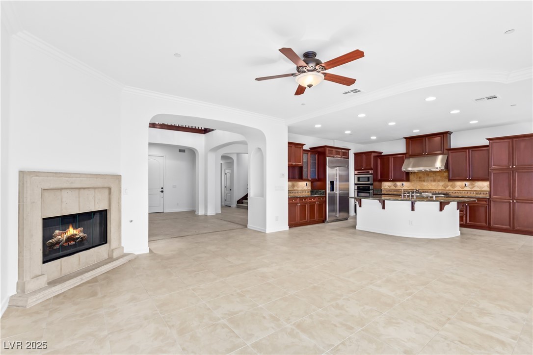 58 Contrada Fiore Drive Henderson, NV 89011 - Photo 18 of 56 Unfurnished living room featuring arched walkways, a tile fireplace, ceiling fan, recessed lighting, and crown molding