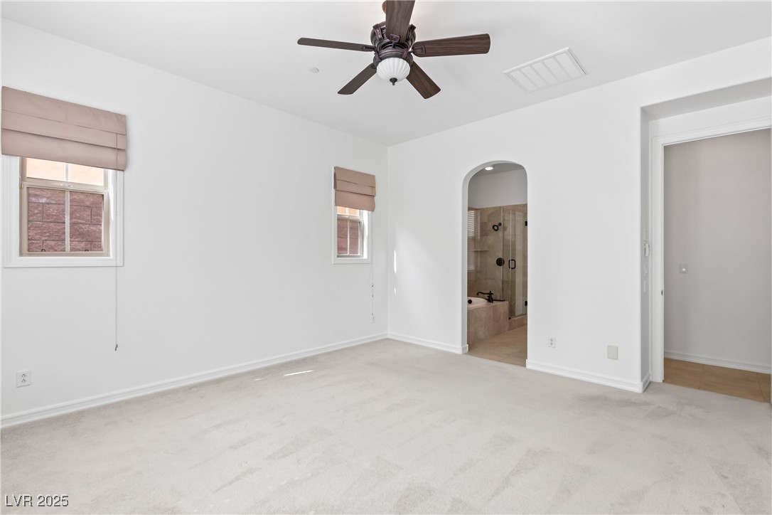 58 Contrada Fiore Drive Henderson, NV 89011 - Photo 21 of 56 Unfurnished bedroom featuring multiple windows, light carpet, a ceiling fan, and arched walkways