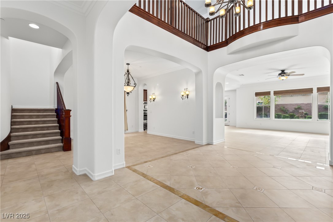 58 Contrada Fiore Drive Henderson, NV 89011 - Photo 6 of 56 Unfurnished room featuring light tile patterned floors, a high ceiling, crown molding, arched walkways, and stairway